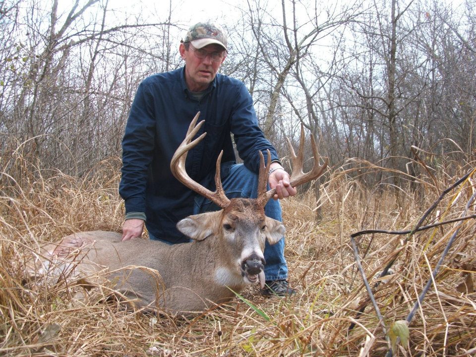 A man wearing glasses grabbing a dead deer by the antlers
