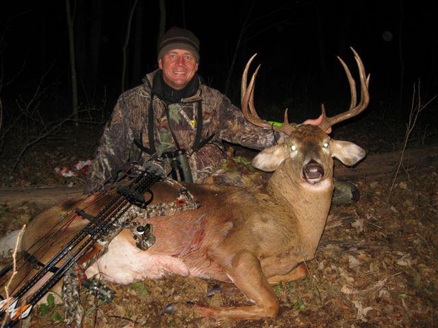 A man in a camouflage jacket posing with a dead deer