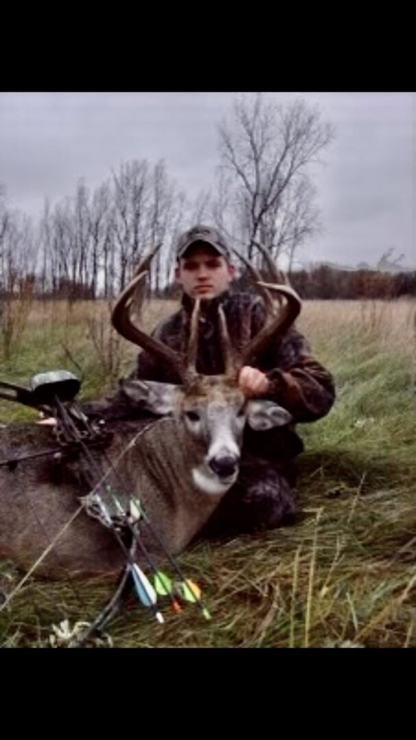 A man with a hunting rifle posing with a dead deer