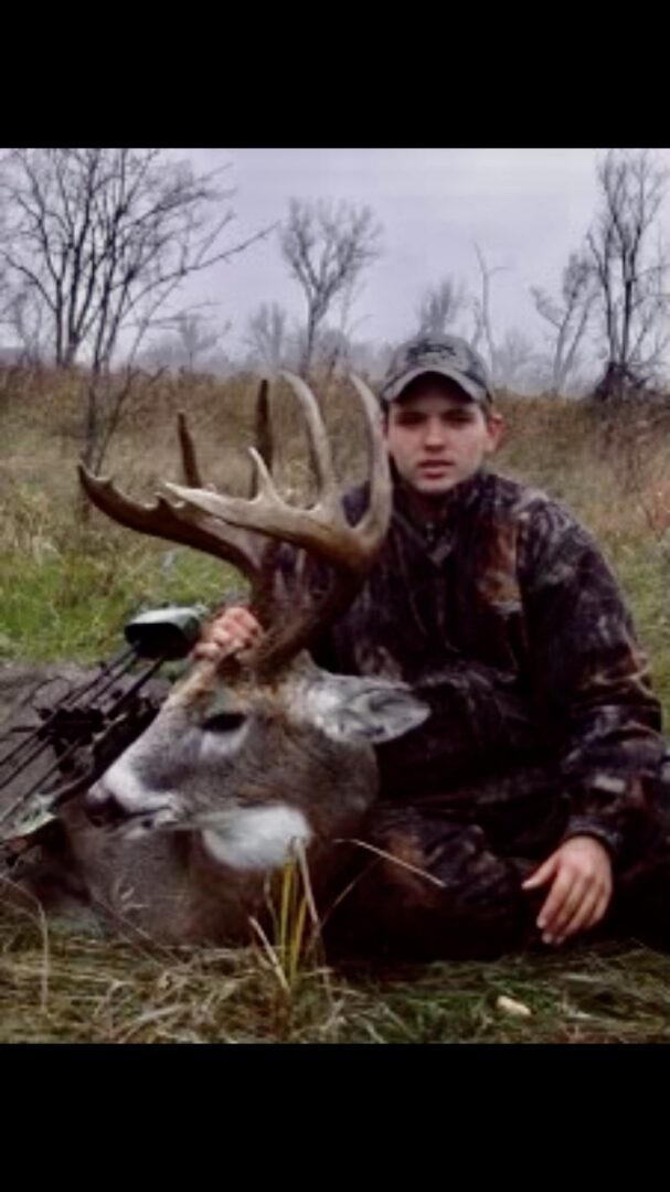 A man with a hunting rifle posing with a dead deer