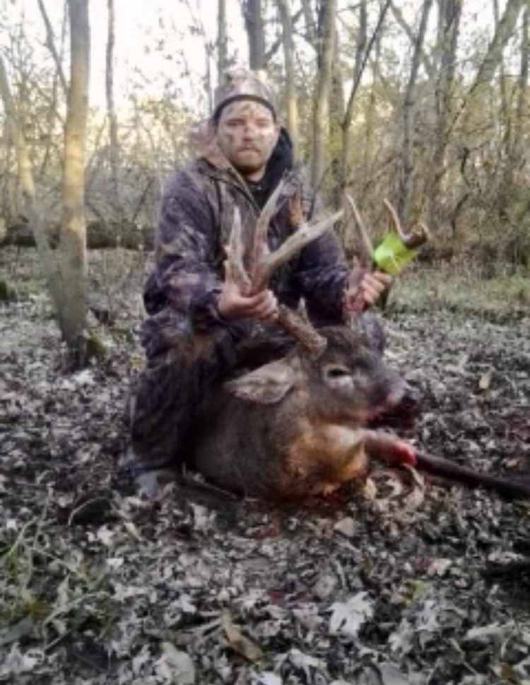 A man with face paint holding a dead deer by the antlers