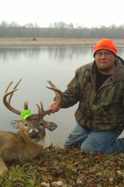 A man in a camouflage jacket posing with a dead deer