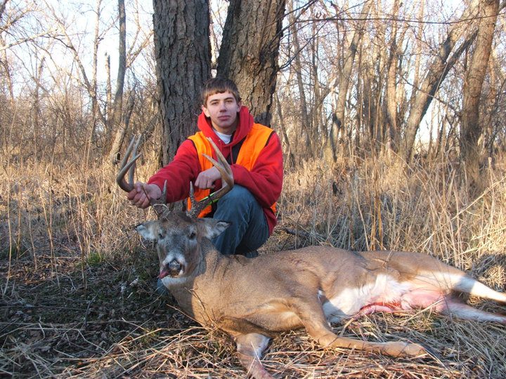 A young man in a hoodie holding a dead deer by the antlers