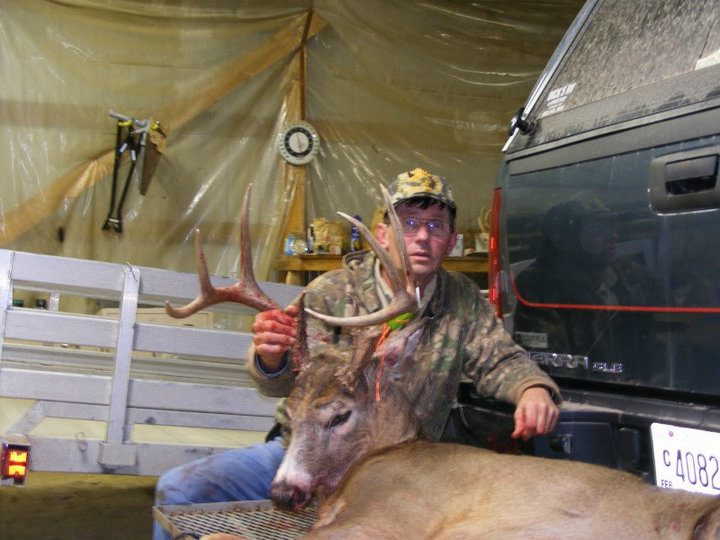 A man with a dead deer behind a pickup truck