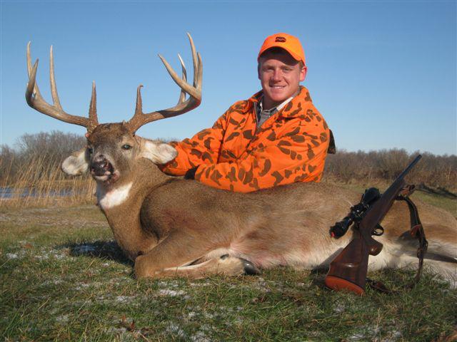 A man in an orange camouflage jacket posing with a dead deer