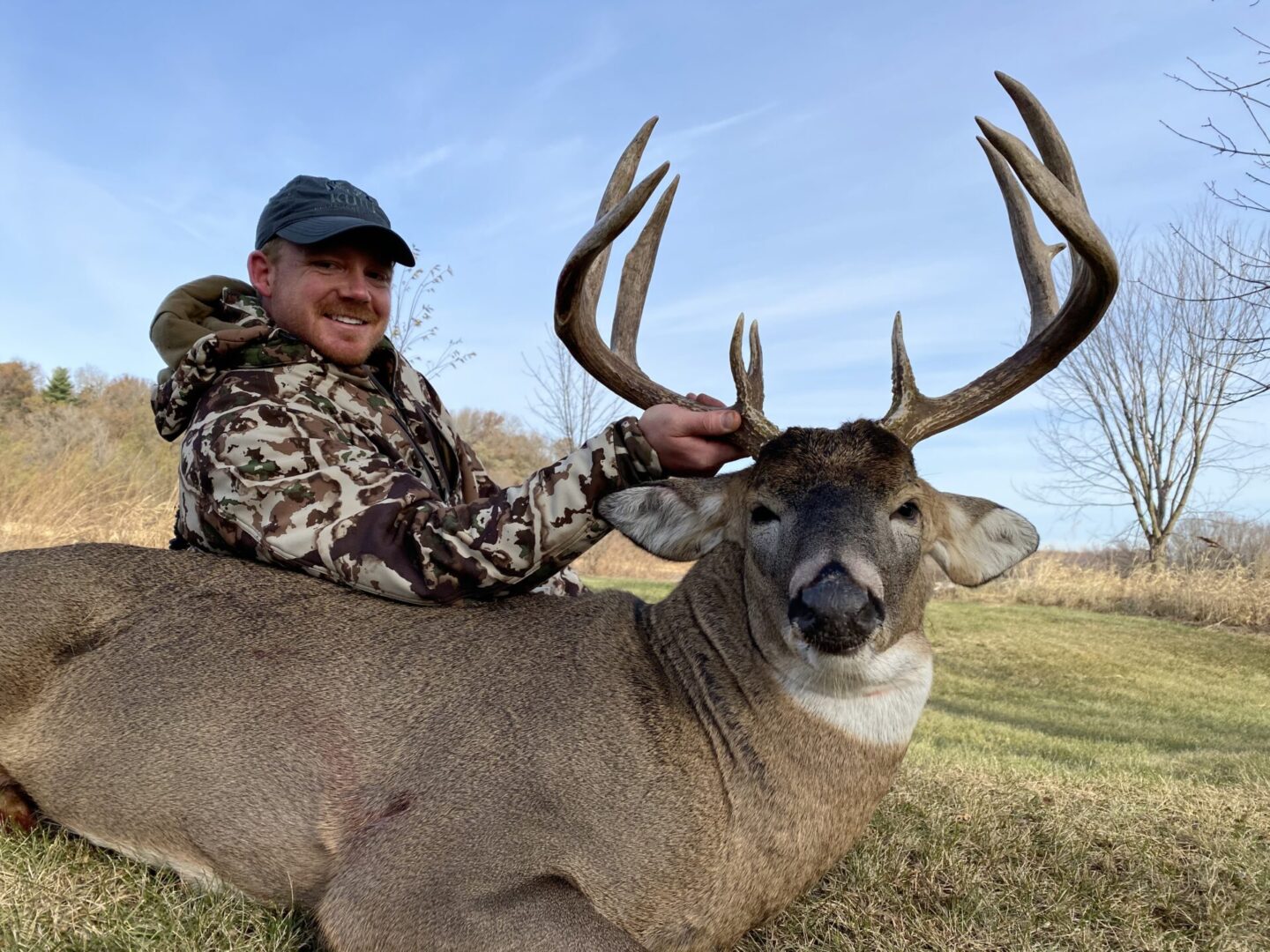 A man with a camouflage jacket holding a dead deer by the antlers